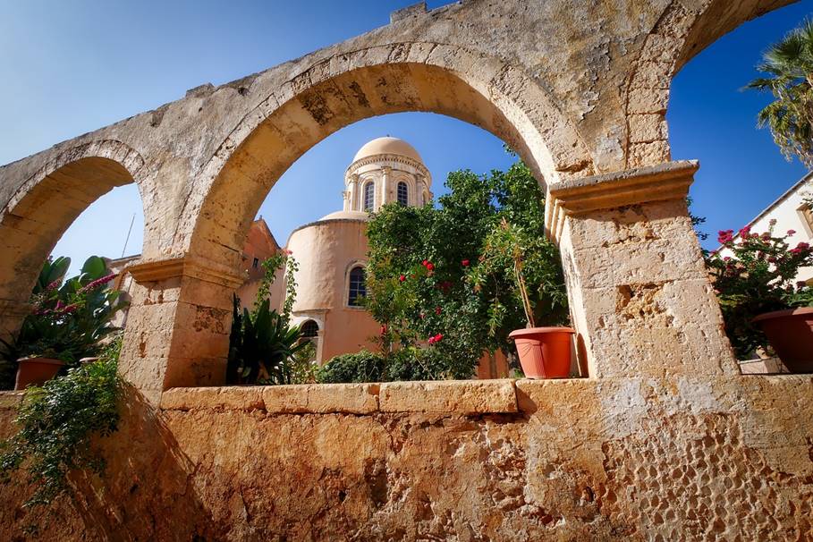 Kreta, miasto na Krecie. Mur, zza którego widać zielone drzewa oraz grecką cerkiew.