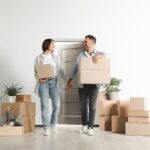 Happy couple with moving boxes entering in new apartment